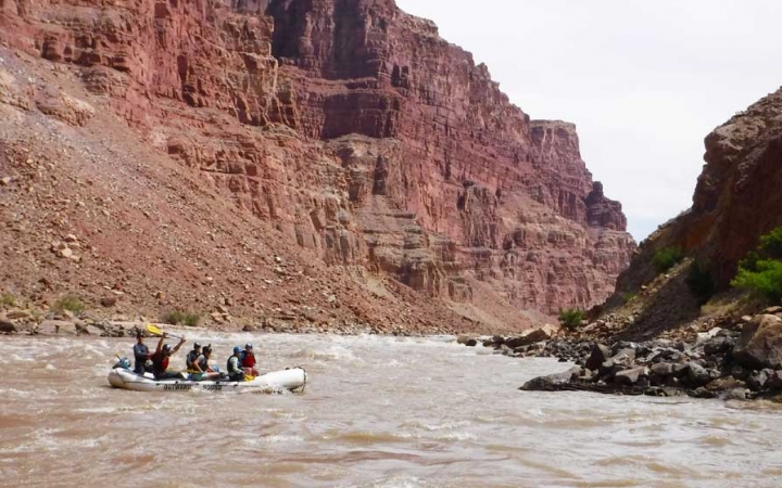 People paddle a raft through whitewater framed by tall canyon walls. 